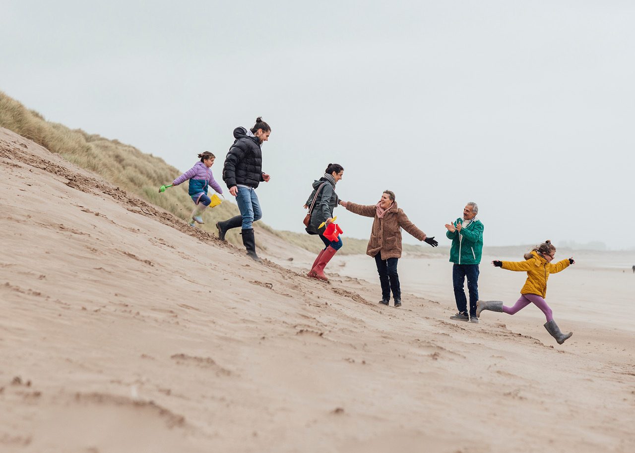 Image of multigenerational family walking down hill on beach